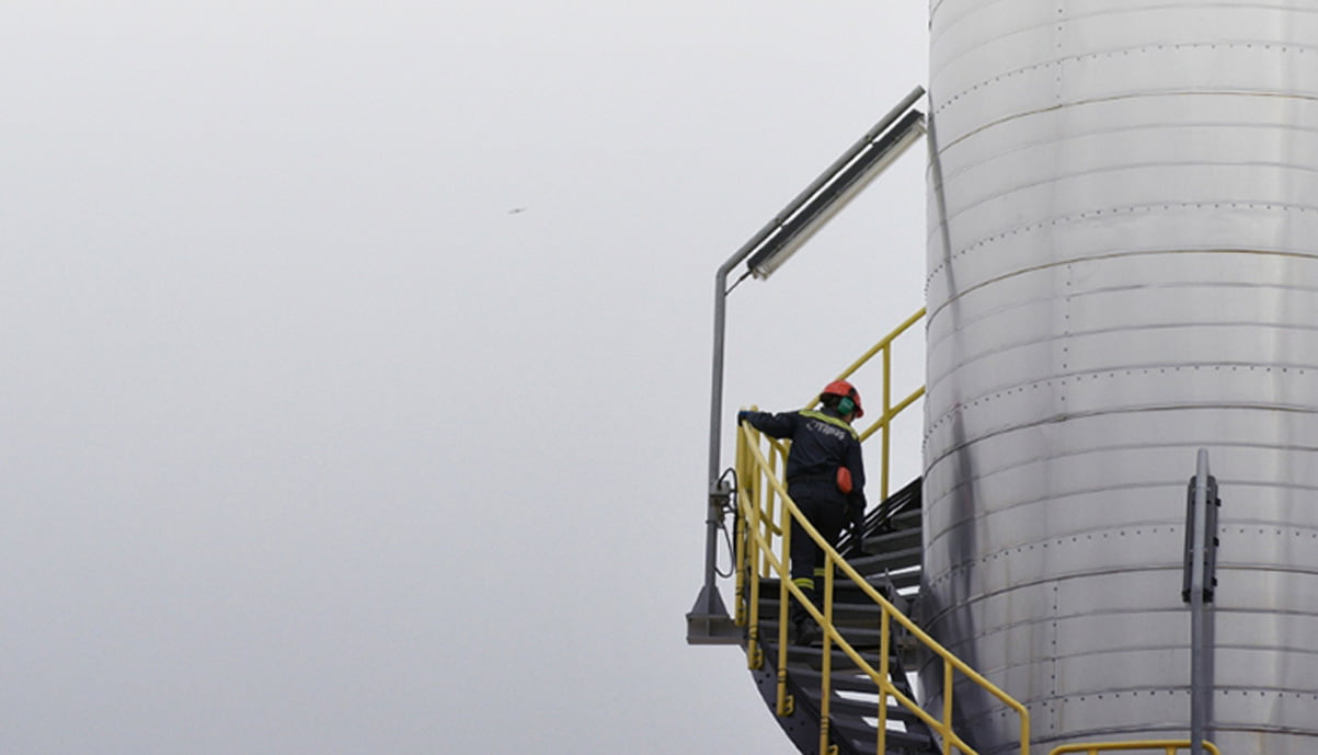 a refinery worker climbing on a high ladder on a very cloudy day